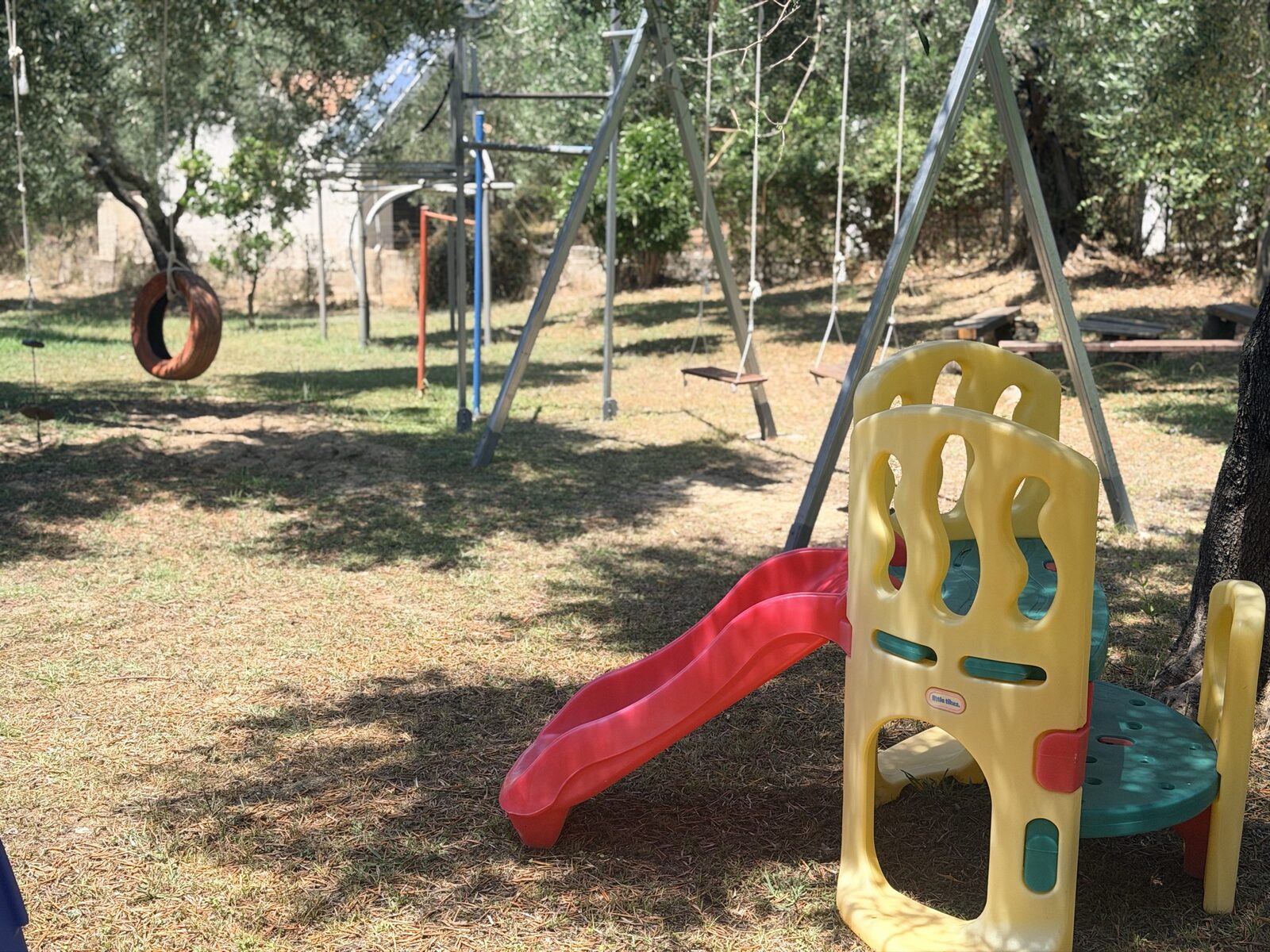 Garden playground with swings and a slide under olive trees at Kalamaki Beach